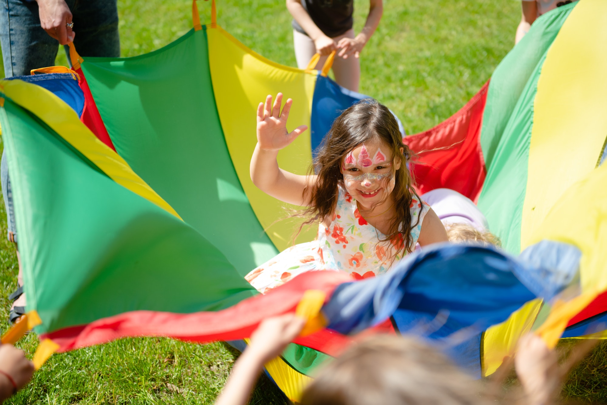 Girl with water make up on her face having fun in multicoloured play parachute on kid’s party.