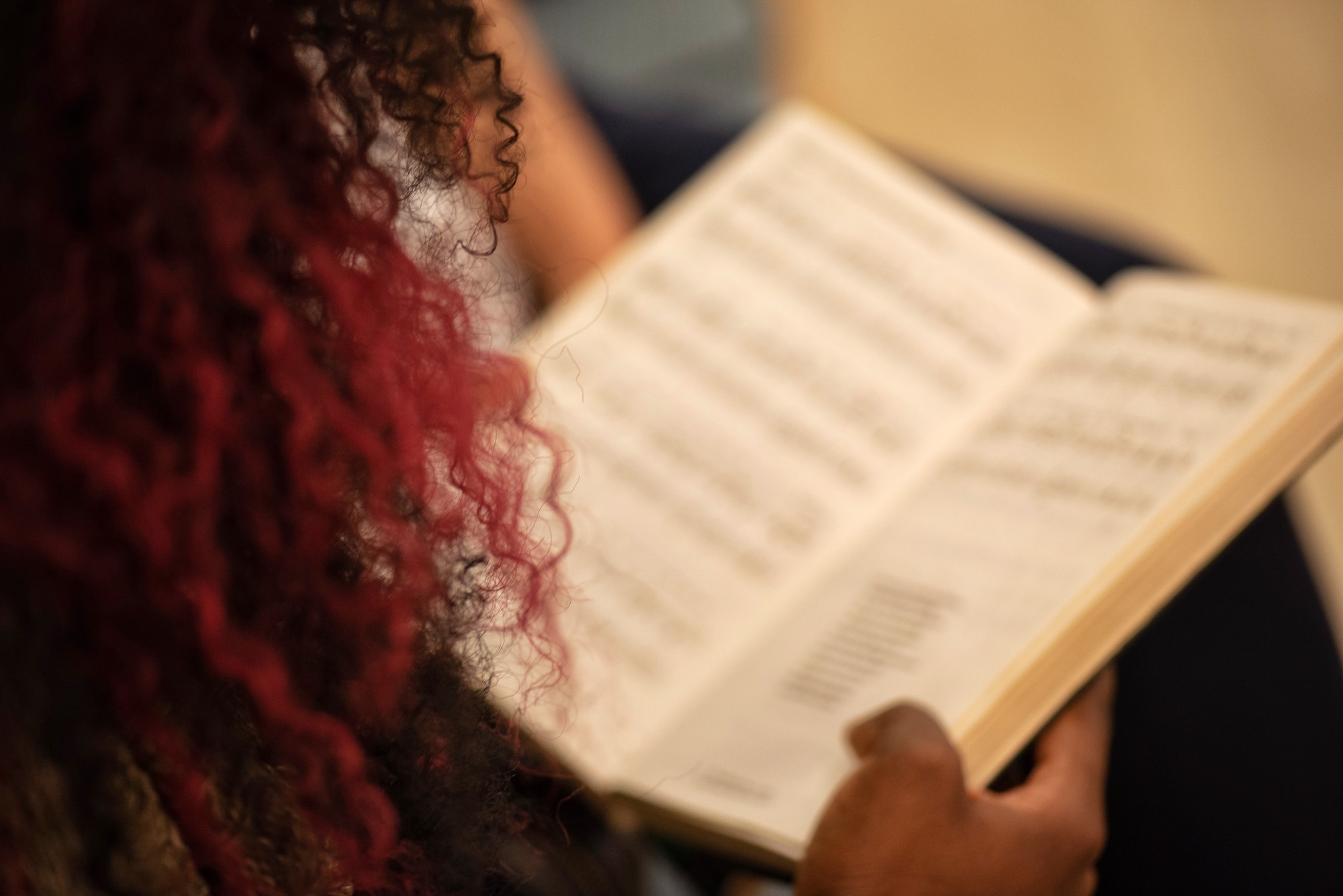 Unrecognizable millennial black woman from behind with curled purple hair singing in a church choir