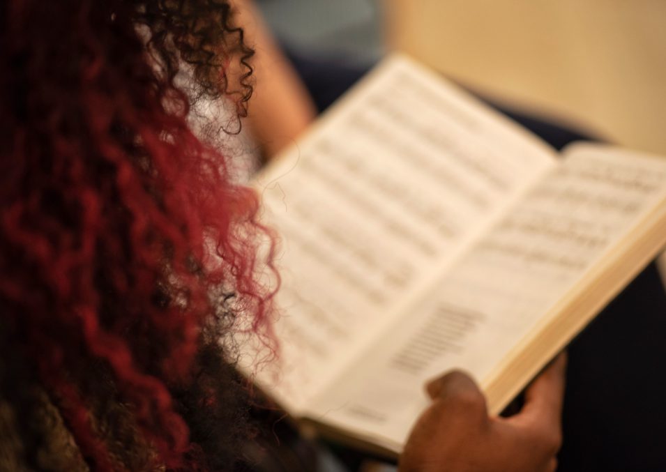 Unrecognizable millennial black woman from behind with curled purple hair singing in a church choir